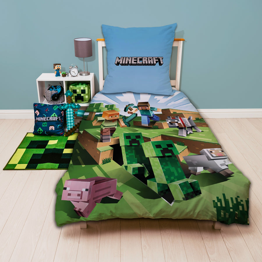 Vorderseite Minecraft Bettwäsche mit wichtigen Charakteren auf grün blauem Grund aufs Bett gezogen und Minecraft Schriftzug auf Kopfkissen