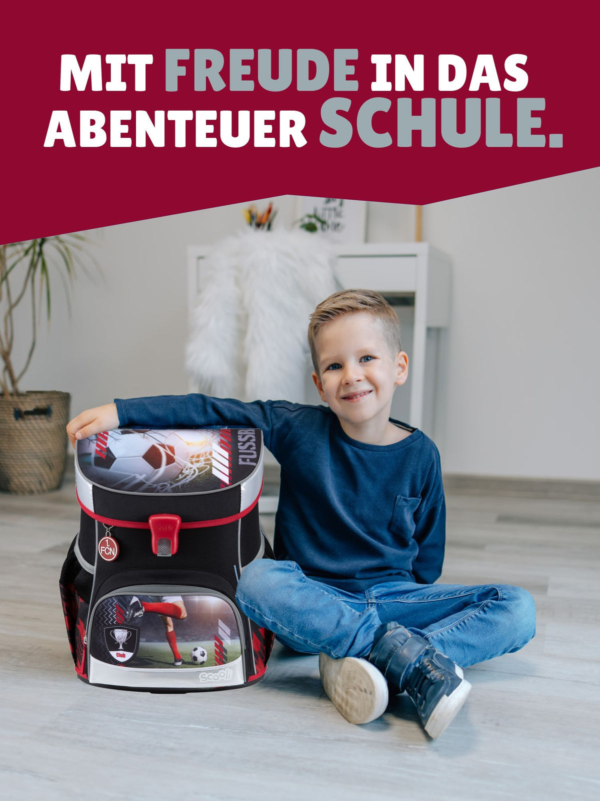 Jungen sitzt neben Schulranzen mit Spruch-Banner "Mit Freude in das Abenteuer Schule"