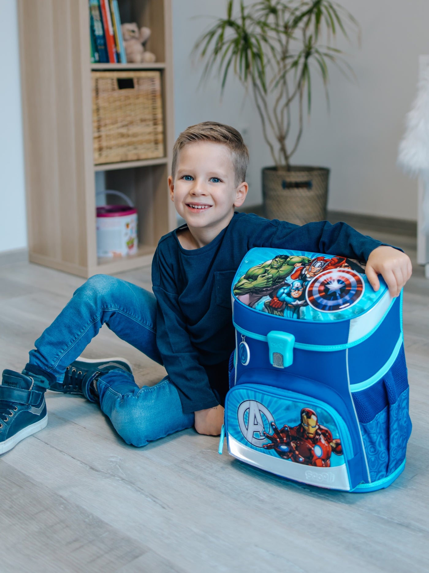 Kleiner Jungen sitzt stolz neben seinem Avengers Schulranzen