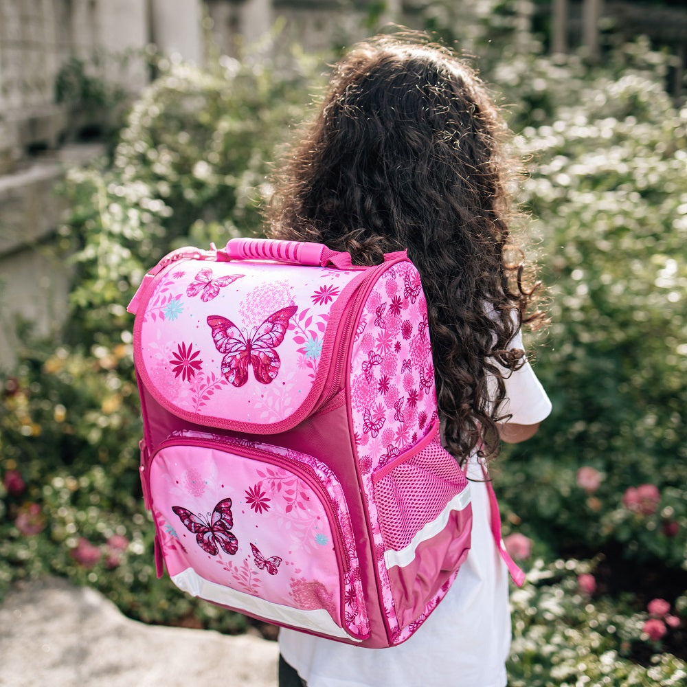 Mädchen mit dunklen Locken trägt den Schmetterling Schulranzen auf dem Rücken