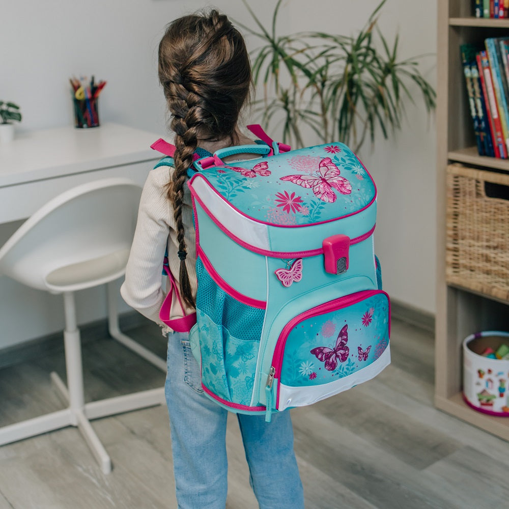 Mädchen sitzt im Wohnzimmer mit Händen auf Schulranzen gestützt und lächelt