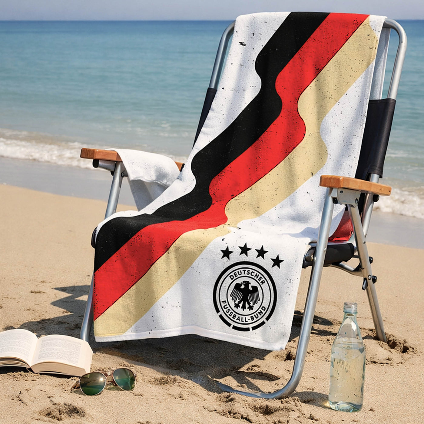 Weißes DFB Handtuch mit schwarz rot gold Streifen liegt über Stuhl am Strand