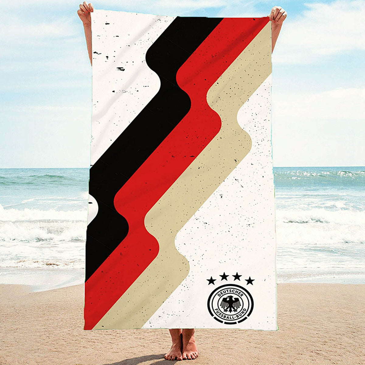 Weißes DFB Handtuch mit schwarz rot gold Streifen und schwarzen Sprenkeln wird am Strand präsentiert
