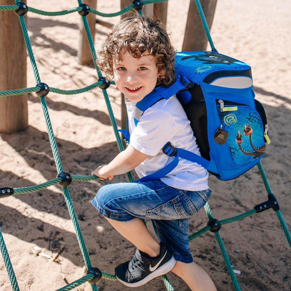 Junge mit Locken trägt den Dragons Schulranzen beim Klettern auf dem Spielplatz