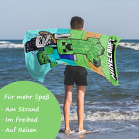 Junge hält Strandtuch hinter Rücken vor Meer 