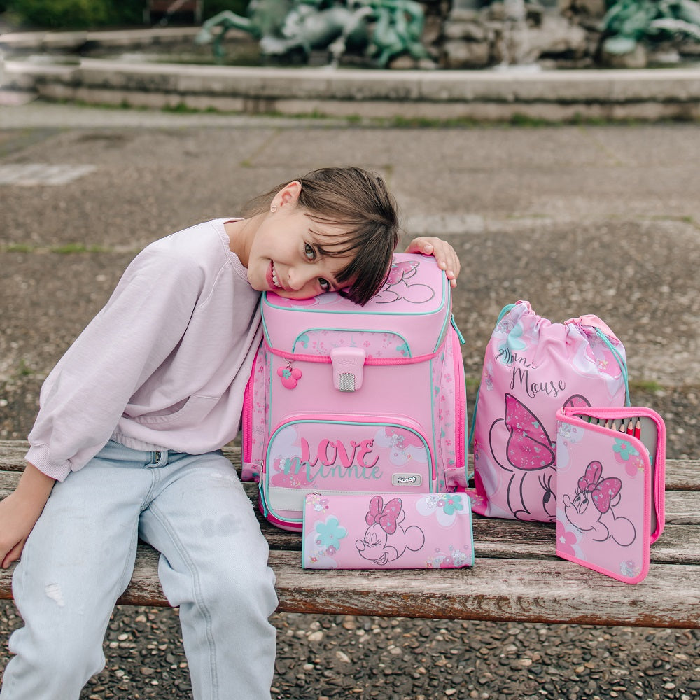 Mädchen sitzt auf Bank mit rosa Minnie Mouse Schulranzenset und lehnt sich auf den Schulranzen