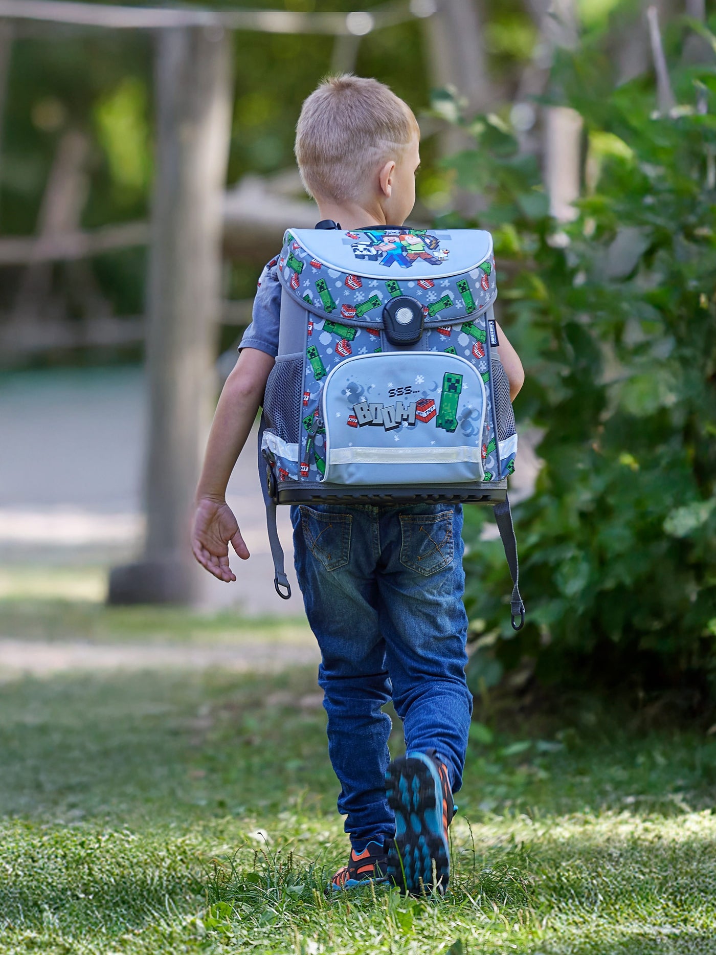 Junge läuft durch Park mit grauem Minecraft Schulranzen auf dem Rücken