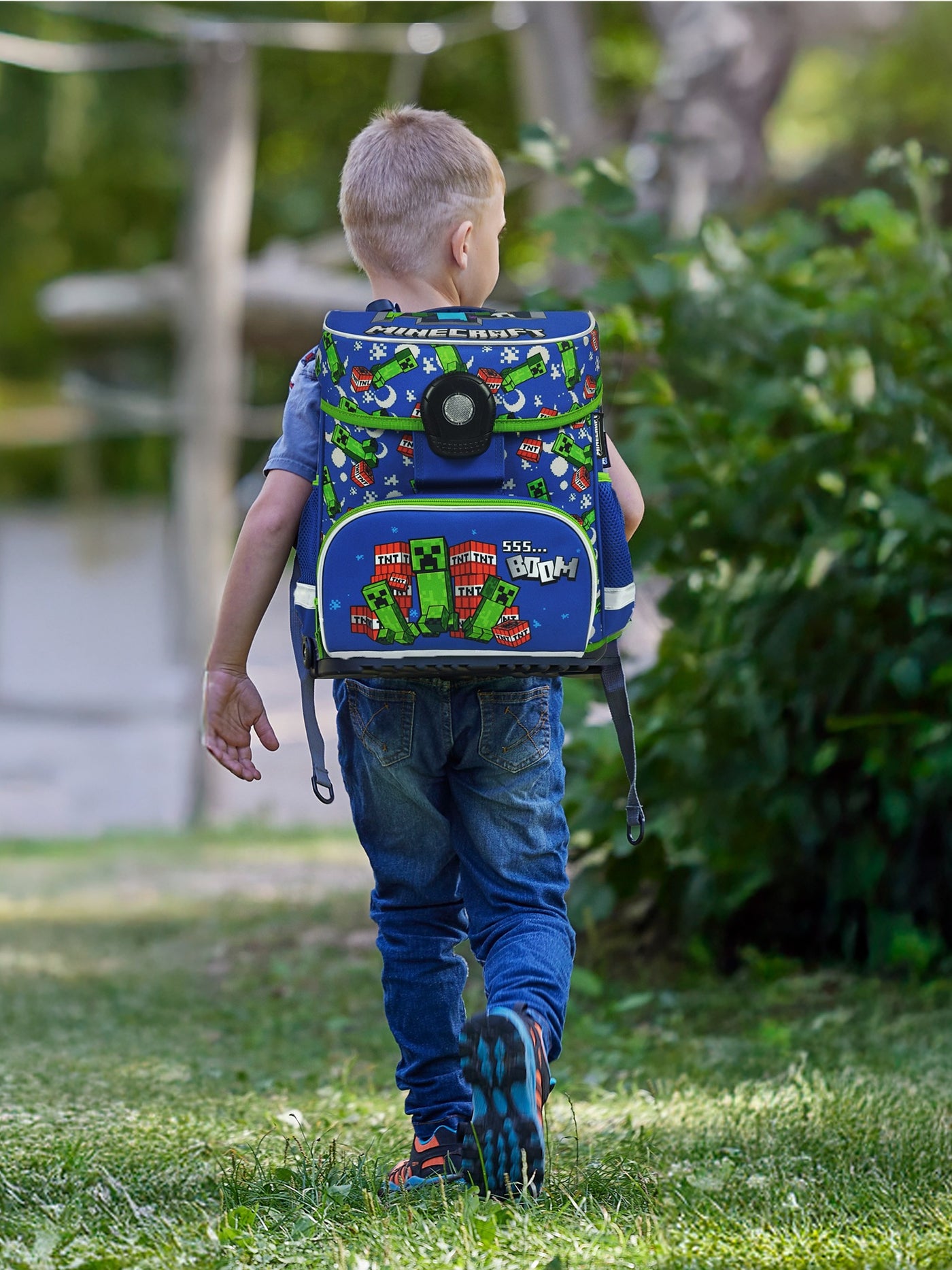 Junge läuft mit blauem Minecraft Schulranzen durch den Park