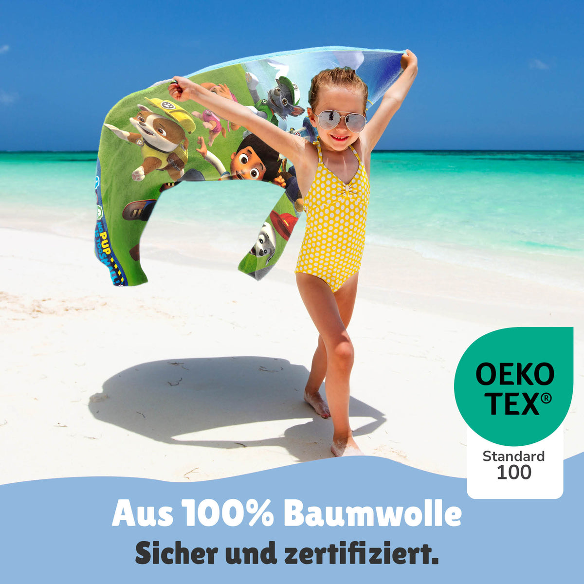 Kleines Mädchen trägt Handtuch an weißem Sandstrand entlang