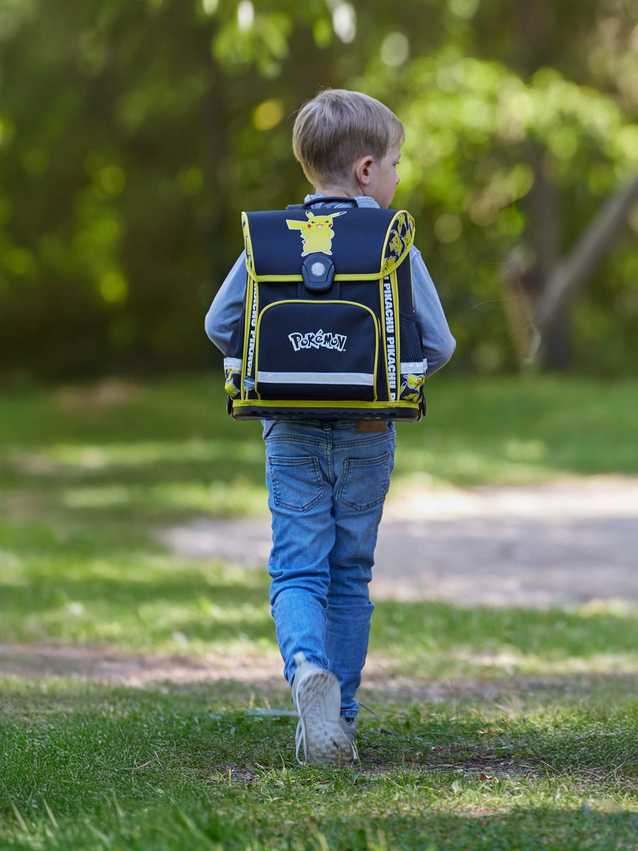 Junge läuft mit schwarz gelbem Pokemon Schulranzen mit Pikachu Motiv durch den Park