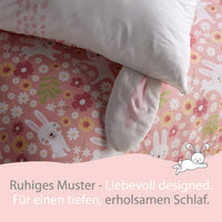 Großaufnahme Kopfkissen mit Ohren und Bettdecke mit rosa Hasen und Blumen Muster darunter