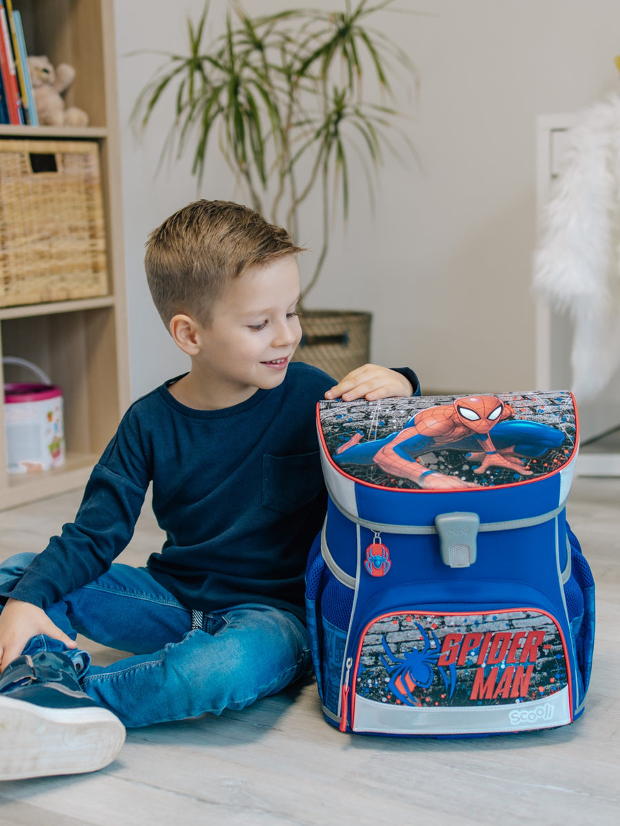 Junge sitzt in hellem Wohnzimmer mit einem Arm auf dem blauen Spiderman Schulranzen