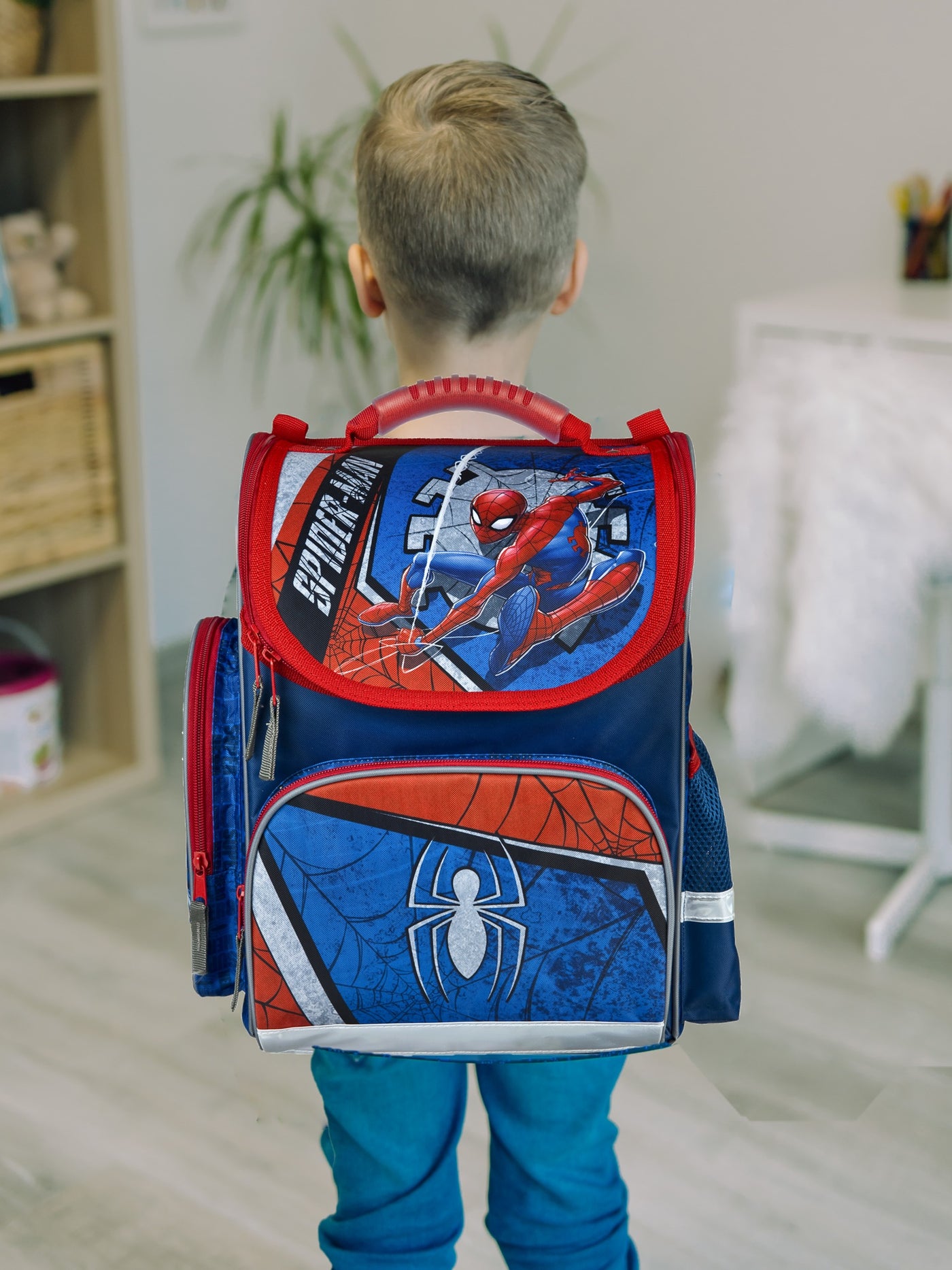 Junge steht in hellem Wohnzimmer mit Spiderman Schulranzen auf dem Rücken