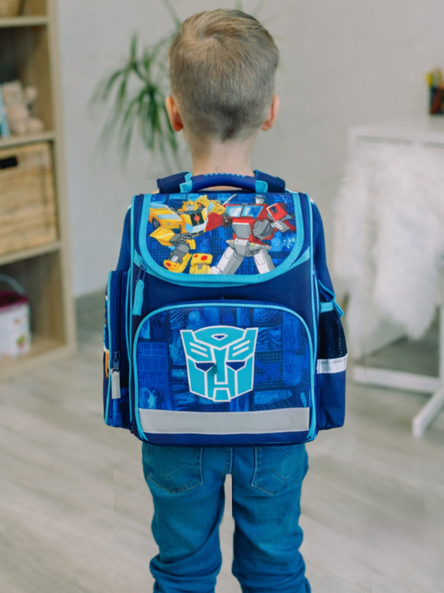 Junge steht mit Rücken zur Kamera und trägt den hellblauen Transformers Schulranzen mit Optimus Prime und Bumblebee auf Deckel am Rücken